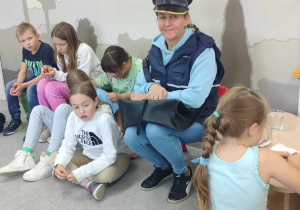 Uczniowie siedzą na dywanie i słuchają pani listonosz.