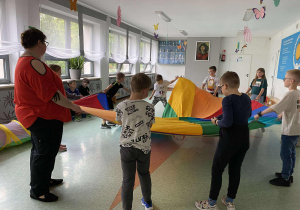 uczniowie z opiekunem bawią się w zabawy ruchowe z chustą animacyjną