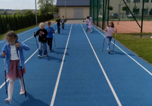 uczniowie na szkolnym boisku spacerują z kijami nordic walking