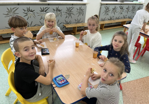 Dzieci jedzą rogaliki z jabłkiem i piją sok jabłkowy