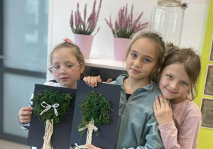 Dziewczynki prezentują wykonane drzewko z mchu i sznurka makramowego.