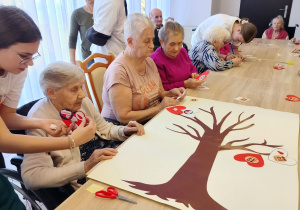 wolontariusze pomagają starszym podopiecznym w przyklejaniu patriotycznych naklejek na biało-czerwone serca