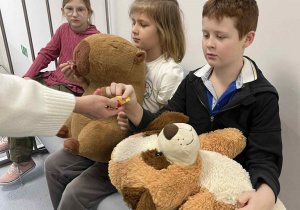 Chłopcy siedzą na pufie trzymając swoje pluszaki