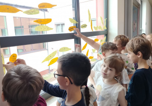 uczniowie przyczepiają do okien papierowe piórka, tworząc wspólną dekorację