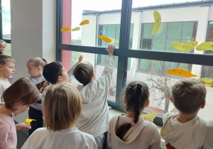 uczniowie przyczepiają do okien papierowe piórka, tworząc wspólną dekorację