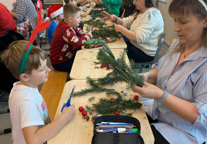 Rodzice wraz z dziećmi tworzą wianki Bożonarodzeniowe.