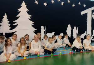 uczniowie klasy 1b z dzwoneczkami pozują na tle scenografii