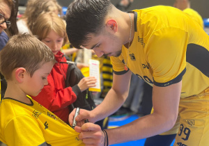 Zawodnik składa autograf na koszulce ucznia