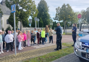 uczniowie klasy 1a na miasteczku ruchu drogowego słuchają policjantów