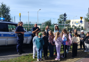 uczniowie klasy 1b na miasteczku ruchu drogowego słuchają policjantów