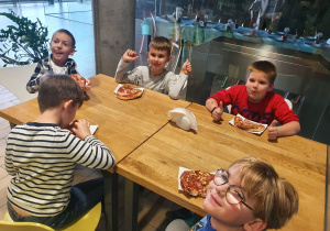 chłopcy ze smakiem jedzą pizzę