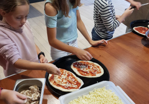 dziewczynki posypują pizze serem