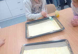 Uczennica smaruje masłem francuskie ciasto.