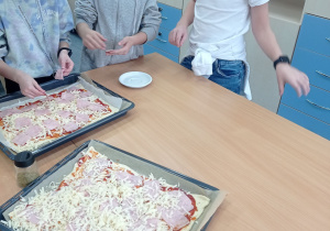 Uczniowie kładą składniki na pizzę.