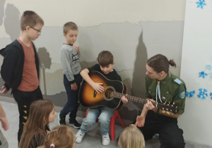Harcerz pokazuję uczniowi grę na gitarze.