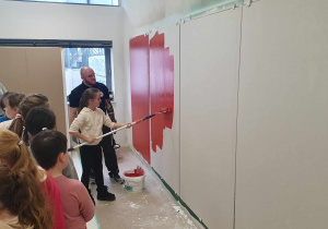 uczennica maluje ścianę czerwoną farbą